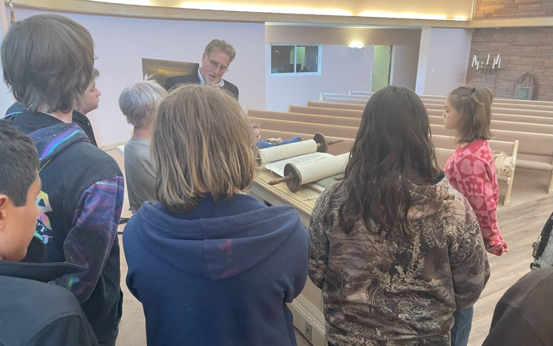 Group of PPOS students standing around a Temple Emanual representative learning about the Torah.